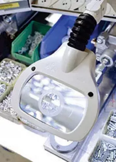 Głowica lampy z&nbsp;lupą Luxo WAVE LED nad drobnymi śrubami i&nbsp;elementami