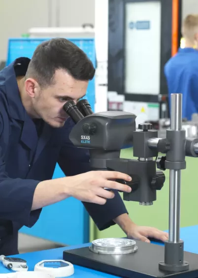 Pracownik kontroli jakości oglądający metalowe elementy na mikroskopie stereoskopowym SX45 Elite